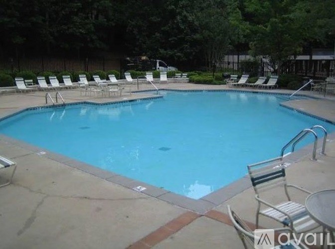 A pool surrounded by chairs and trees.