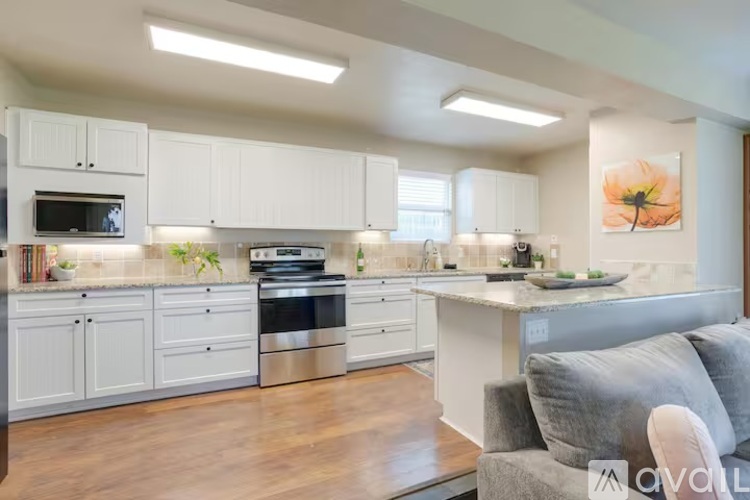 A modern kitchen with white cabinets and a grey couch.