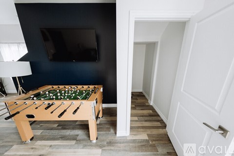 A pool table with a green cloth and white balls is in the foreground of a room with a television and a white door.