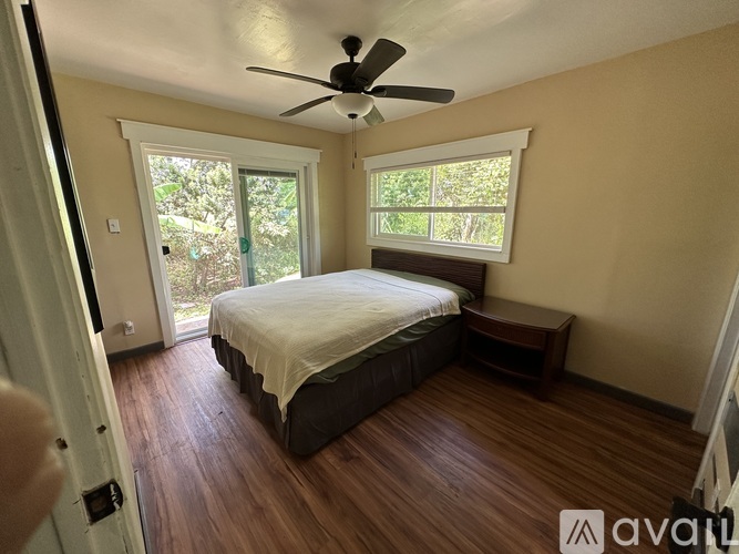 A bedroom with a bed, a ceiling fan, and a window with a view of the outdoors.