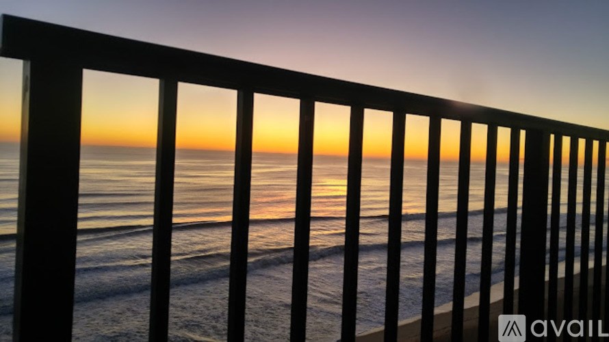 A railing overlooks a beach at sunset.