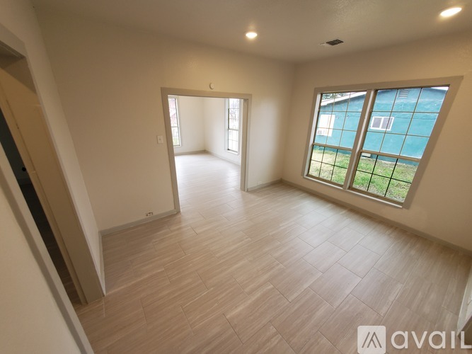 A spacious room with wooden flooring and large windows.