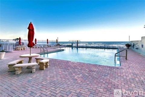 A pool area with a red umbrella and benches.