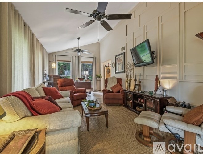 A living room with a white couch, red pillows, and a ceiling fan.