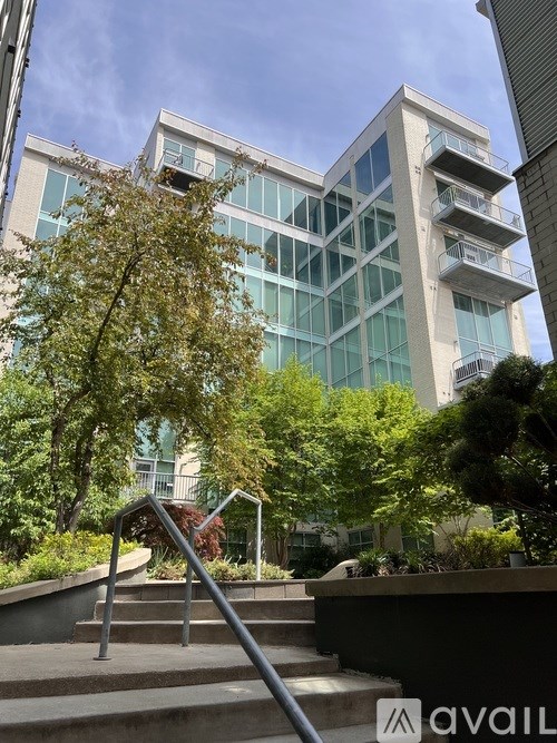 A modern building with glass windows and balconies is surrounded by trees and greenery.