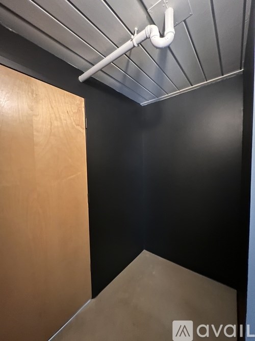 A white pipe hangs from the ceiling in a room with a wooden door.