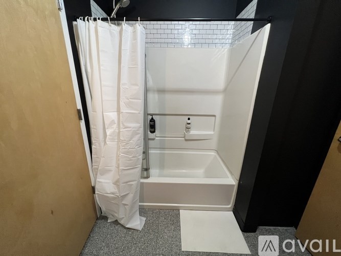 A white shower stall with a white shower curtain and a white mat on the floor.