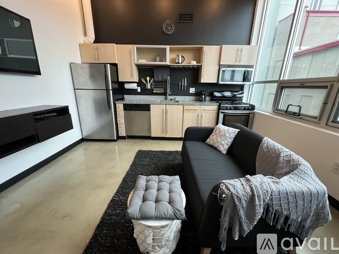 A modern kitchen with a black fridge and a black couch with a grey blanket on it.