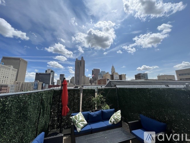 A red umbrella is on a blue couch on a balcony with a city skyline in the background.