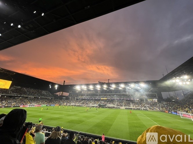 A packed stadium is watching a soccer game under a sunset sky.