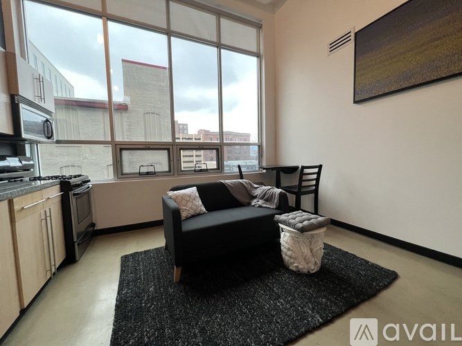 A living room with a black couch and a large window overlooking a cityscape.