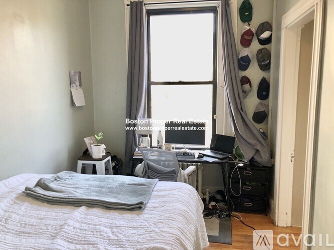 A bedroom with a bed, desk, and window with curtains.