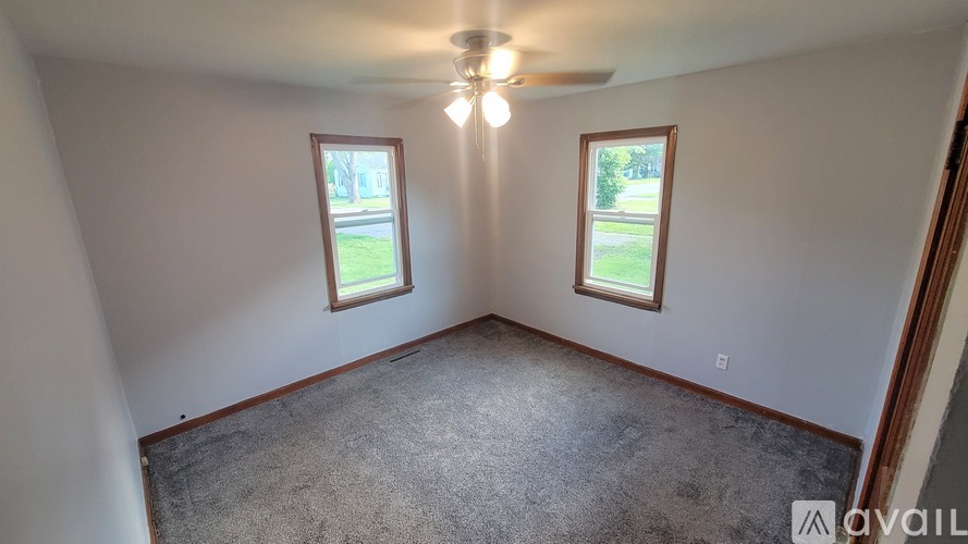 A room with a ceiling fan and two windows.