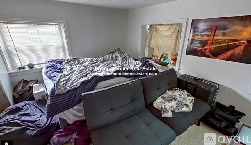 A room with a couch, a bed with a blue blanket, and a picture of a bridge on the wall.