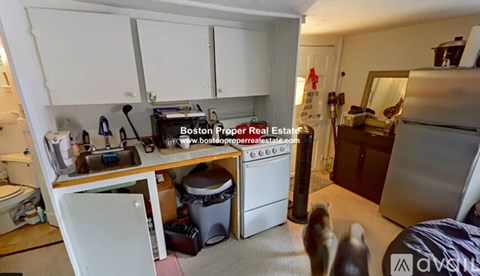 A kitchen with white cabinets and appliances, a fridge, and a counter with a toaster and other items.