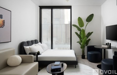 A living room with a grey couch, a black coffee table, a white sofa, a black chair, a black plant, and a painting on the wall.