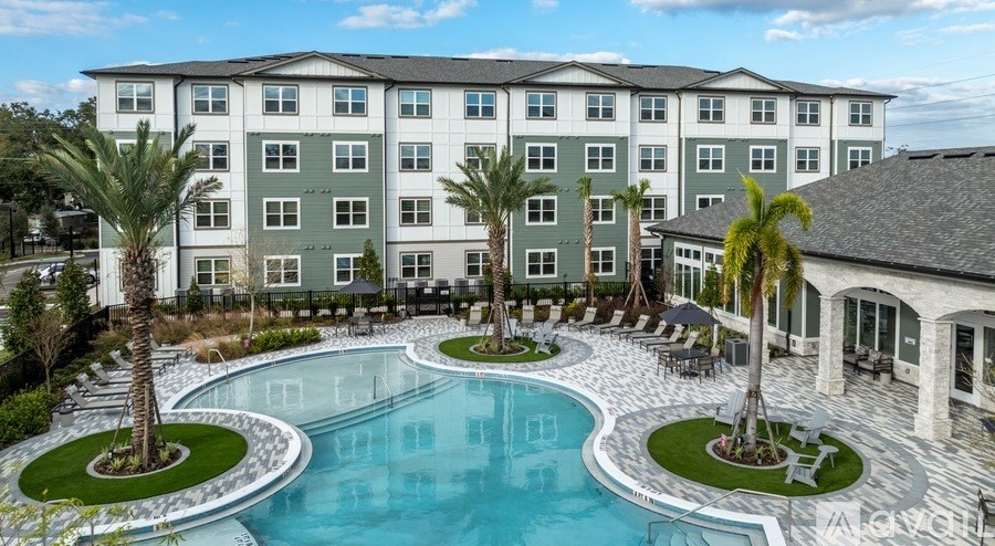 A large swimming pool is surrounded by palm trees and lounge chairs in front of a multi-story apartment building.
