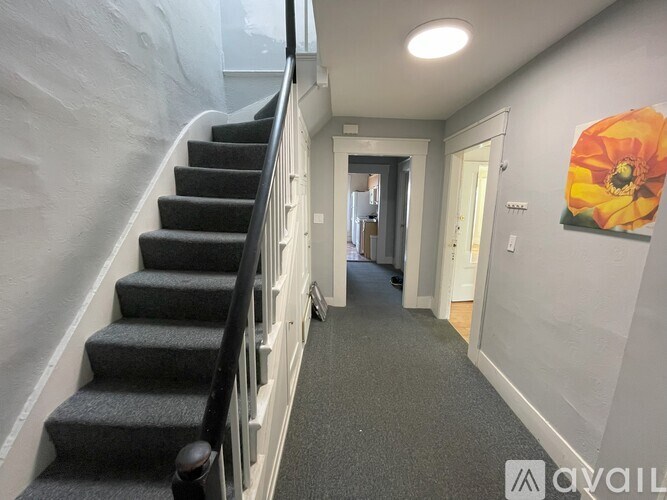 A hallway with a staircase and a flower painting on the wall.