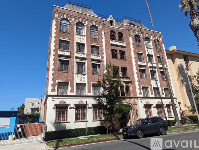 A tall red brick building with many windows and a tree in front.