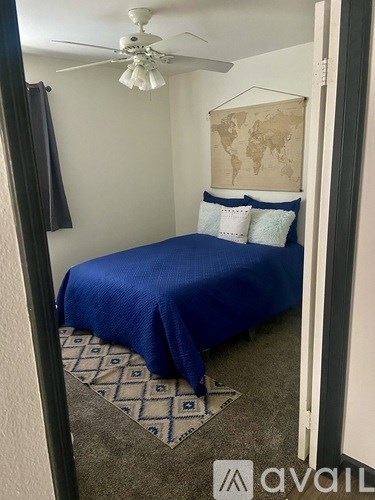 A bedroom with a blue bedspread and a world map on the wall.