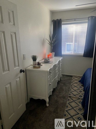 A room with a white door, a small table with a plant and a book on it, and a window with blinds.