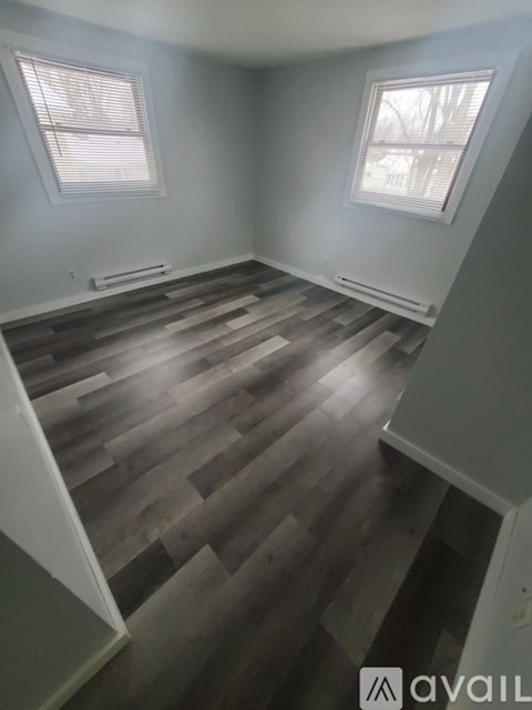A room with wooden flooring and two windows.