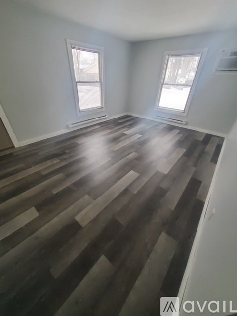 A room with wooden flooring and two windows.