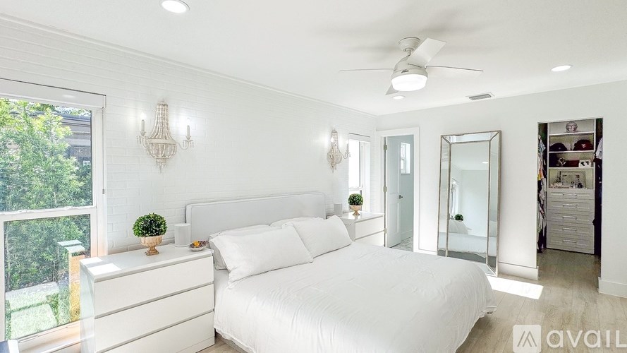A bedroom with a large bed, a chandelier, and a balcony with a view of trees.