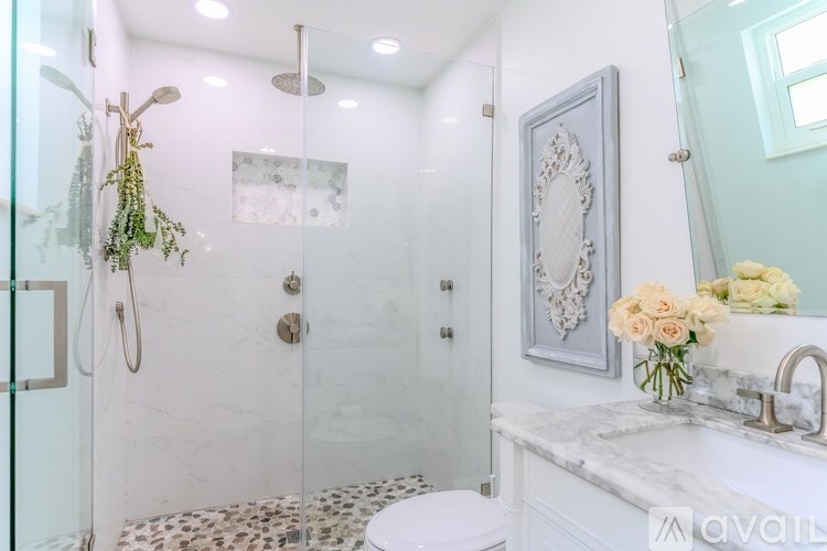 A bathroom with a white toilet, a glass shower stall, and a sink with a vase of flowers.
