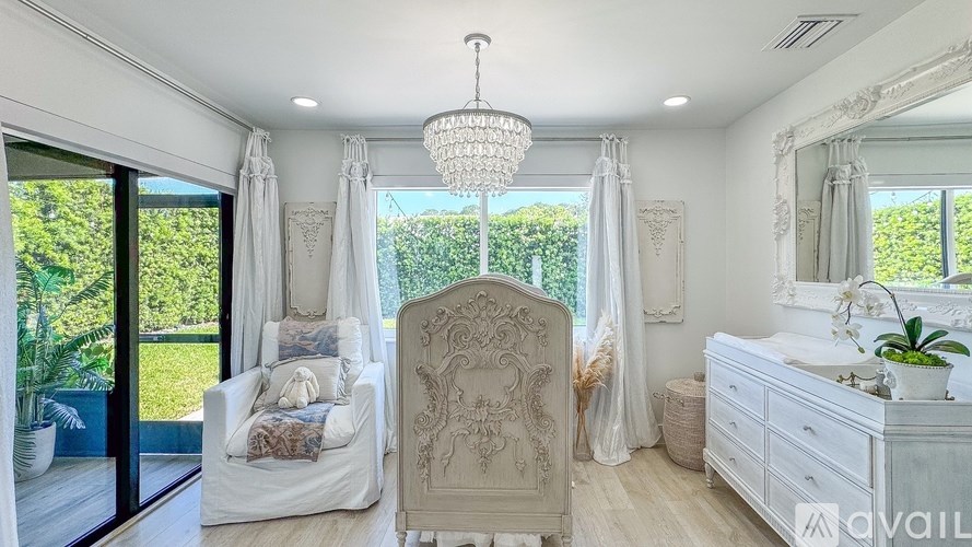 A white bedroom with a large bed, a chair, and a chandelier.