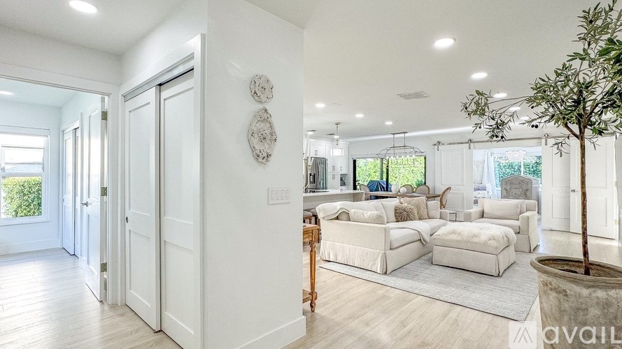 A living room with white furniture and a tree in a pot.