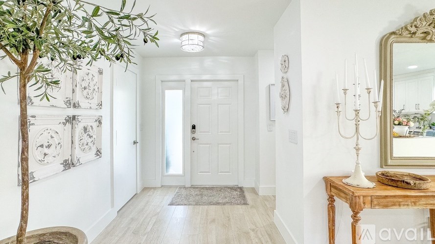 A hallway with a tree, a mirror, and a table with a candle on it.