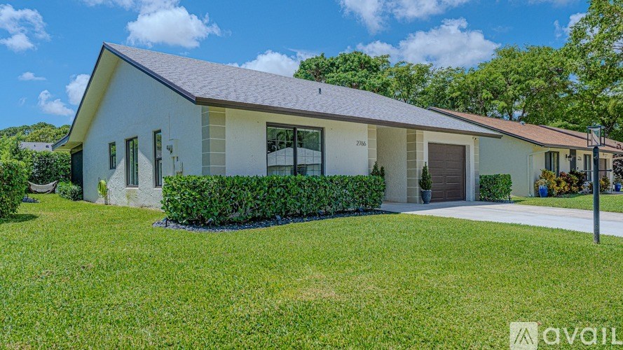 A white house with a grey roof and a sign that says "available" in the front yard.