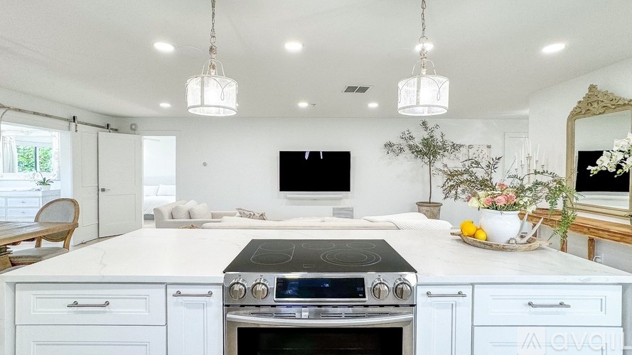 A white kitchen with a black stove top oven and a TV mounted on the wall.