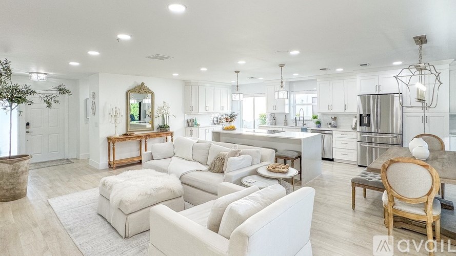A well-lit, spacious living room with white furniture and a neutral color scheme.