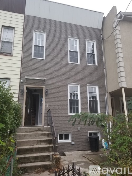 A grey house with a black trash bin in front.