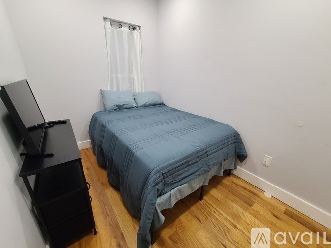 A bedroom with a bed, a television, and a wooden floor.