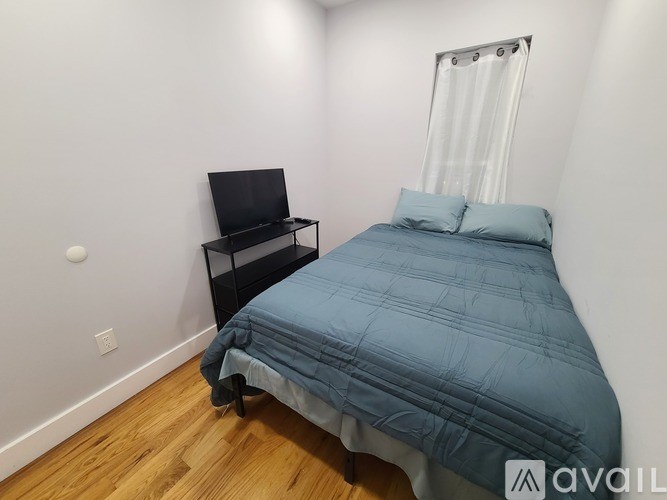 A bed with a blue comforter and a black shelf unit with a television on it.