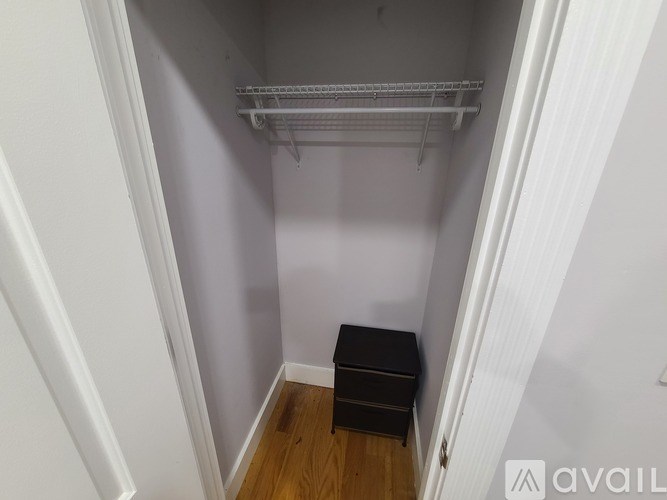 A small closet with a shelf and a black box on the floor.