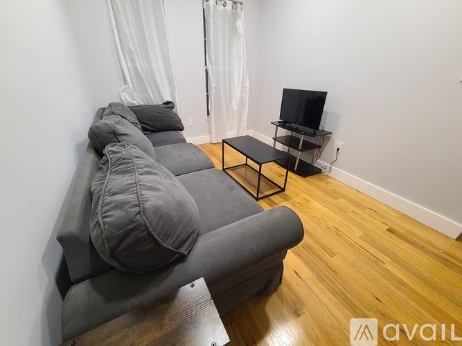 A grey couch with a black TV stand in front of it.