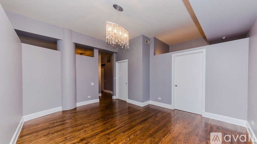 A spacious room with wooden floors and a chandelier hanging from the ceiling.