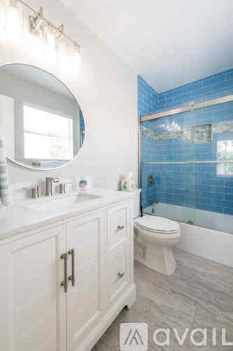 A bathroom with a white vanity and a blue tiled shower.