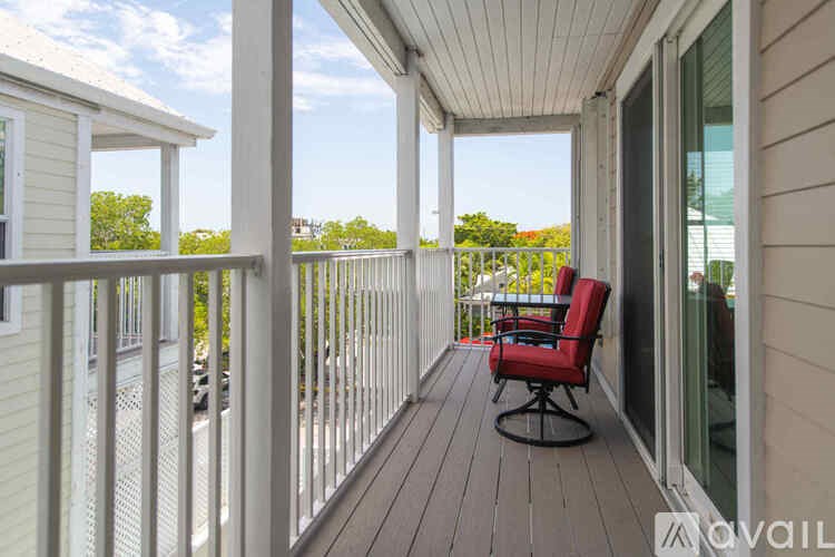 A red chair is on a wooden deck with a white railing.