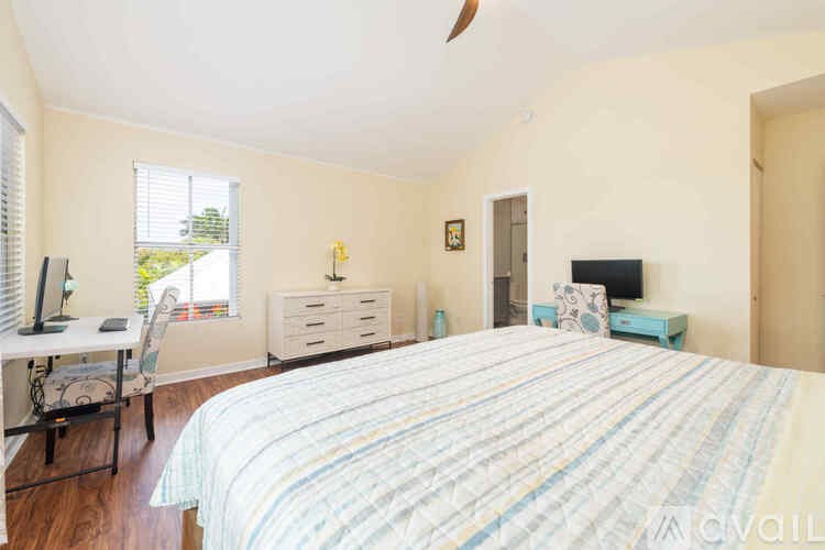 A bedroom with a bed, desk, chair, and a window with blinds.