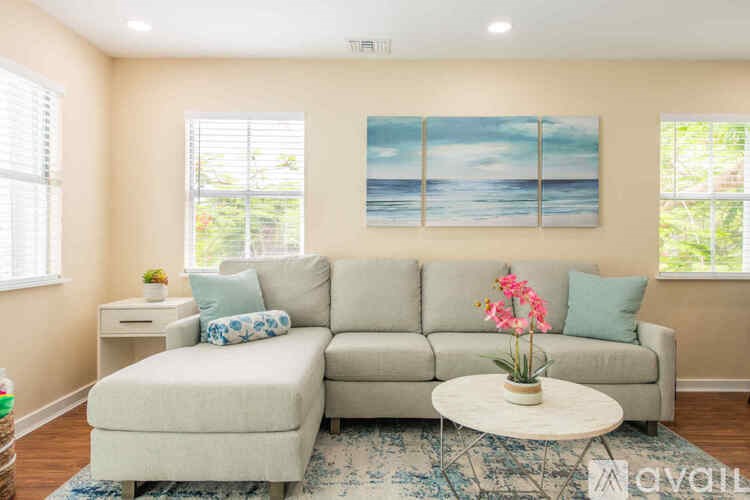 A living room with a grey couch, a white coffee table, and a painting of a beach scene on the wall.