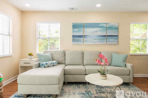 A living room with a grey couch, a white coffee table, and a painting of a beach scene on the wall.