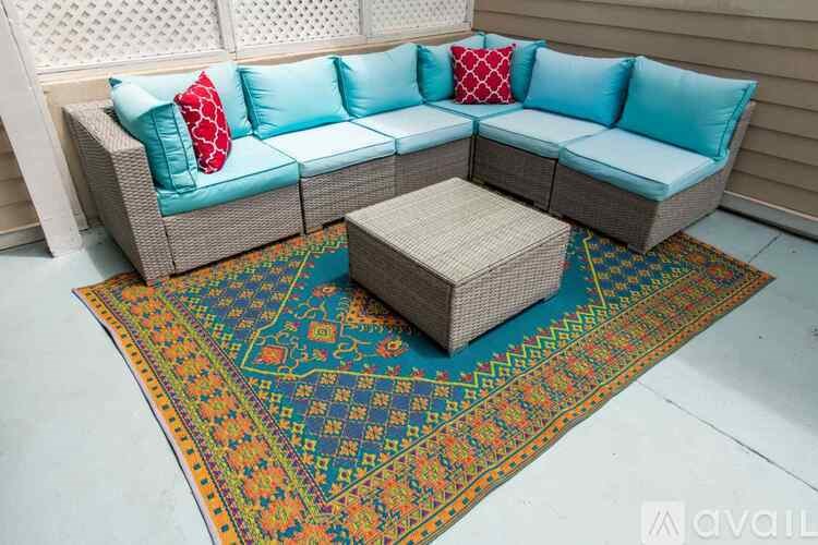 A sectional sofa with a woven ottoman and a colorful rug in front.