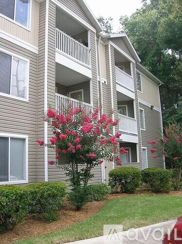 A building with a balcony and a tree with pink flowers in front.
