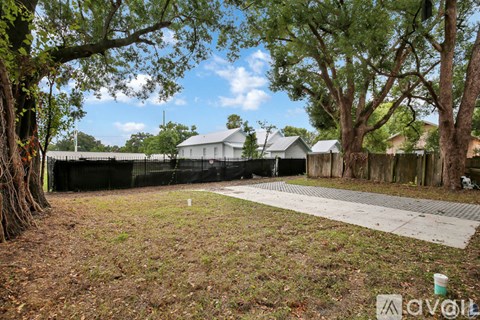 A yard with a fence and a tree in front of a house.