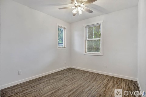 A room with a ceiling fan and two windows.